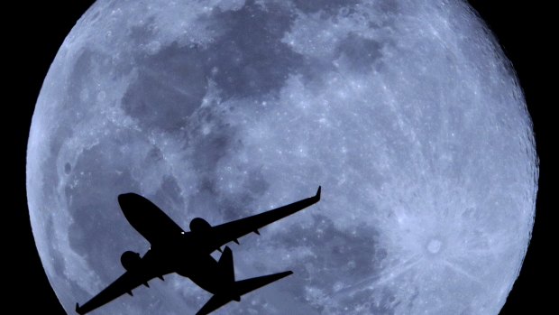A passenger jet is silhouetted against the rising full moon as it takes off from Sky Harbor airport in Phoenix. 