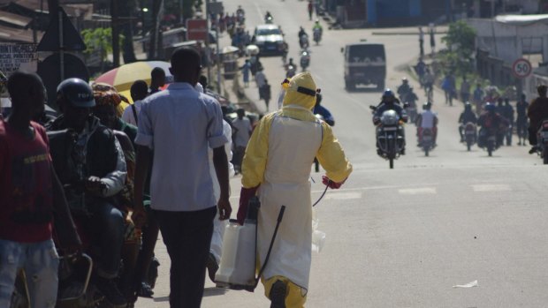 Panic: A health worker with disinfectant spray walks down a street outside the government hospital in Kenema, Sierra Leone.