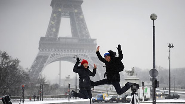 Two Japanese tourists in front of the snow-covered Eiffel Tower.