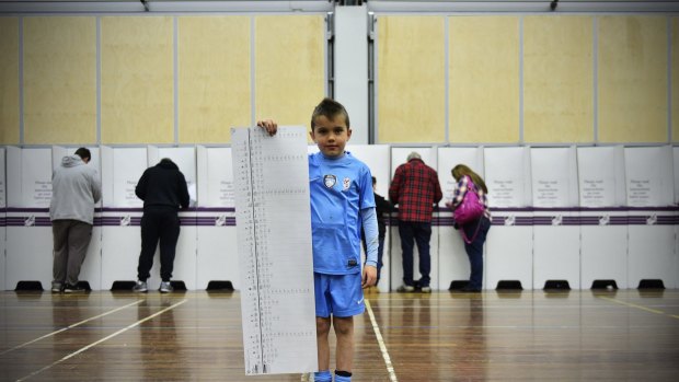 A young boy holds a Senate ballot paper for his parents on election day.