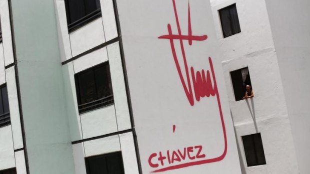 A woman stands at a window of a building bearing a design of the signature of late Venezuelan President Hugo Chavez in Ciudad Caribia outside Caracas.
