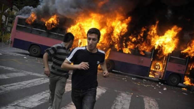 Opposition fury ... supporters of the defeated candidate Mir-Hossein Mousavi run past a burning bus on Saturday.