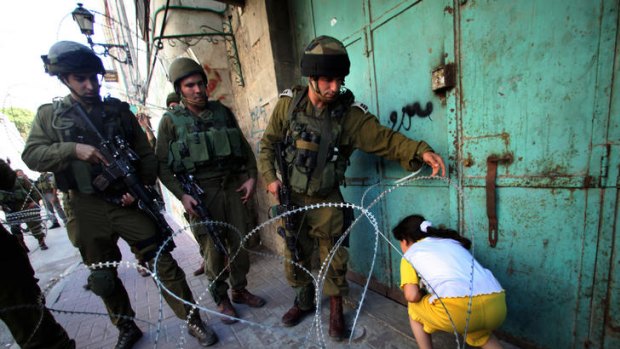 Israeli soldiers let a Palestinian girl make her way past a barbed wire barricade set up to prevent protesting Palestinians from accessing an Israeli settlement, in Hebron on the West Bank.