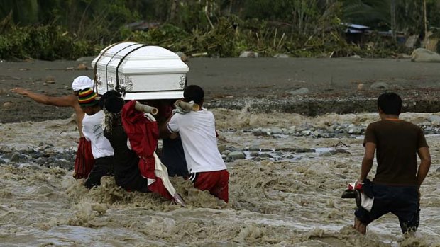 Wake of the storm ... relatives cross a river to bury a flood victim in the southern Philippines.