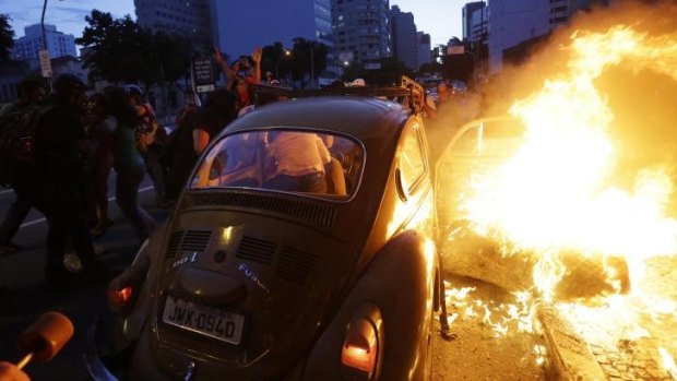 A woman gets out of a car which caught fire when the driver tried to drive past a burning barricade in Sao Paulo, Brazil.
