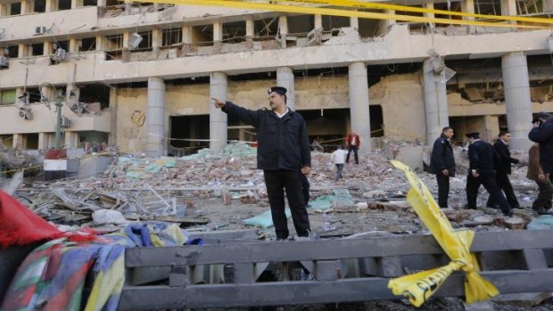 Deadly strike: A police officer orders people back from the scene of the car bomb attack on police headquarters in Cairo on Friday.