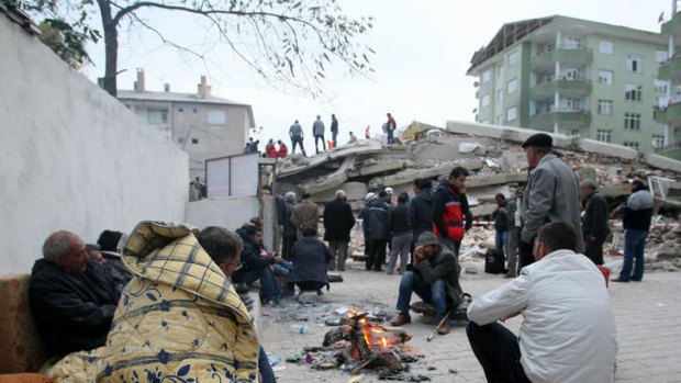 Survivors of the earthquake warm up as rescuers search the debris of collapsed buildings in the eastern Turkish town of Ercis.