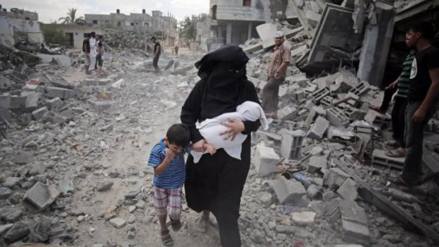 A Palestinian woman passes by rescuers inspecting the rubble following Israeli strikes on the Rafah refugee camp.