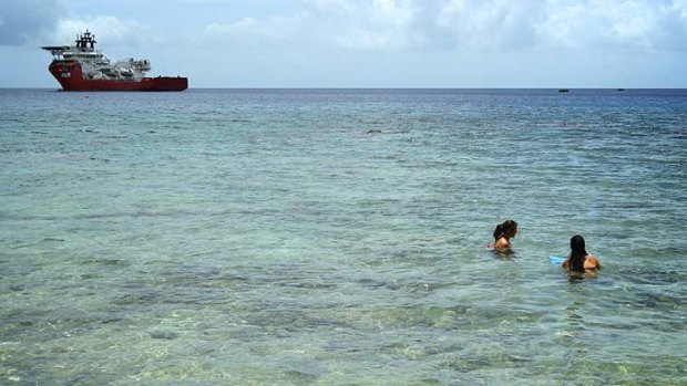 Customs vessel Ocean Protector waits in Flying Fish Cove, Christmas Island, as tourists snorkel in the shallow waters.