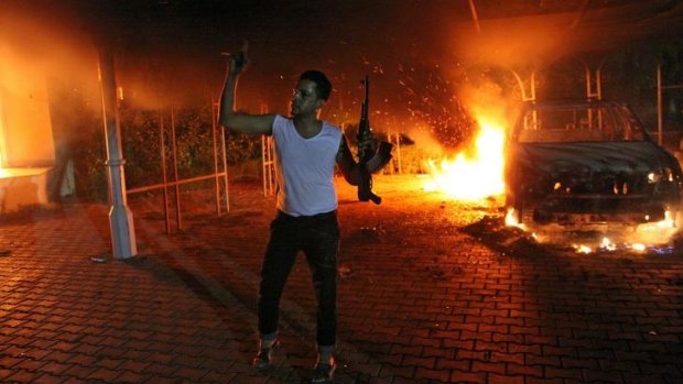 An armed man waves his rifle as buildings and cars are engulfed in flames after being set on fire inside the US consulate compound in Benghazi late on September 11, 2012. A US Senate committee has found the compound was poorly protected.  
