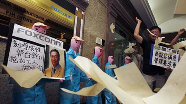 Protesters from several workers' rights groups throw paper money in front of paper figures, depicting workers who recently died in apparent suicides, during a traditional Chinese mourning ceremony outside a Foxconn office in Hong Kong.