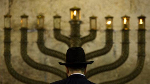 An Ultra-Orthodox Jewish man stands in front a menorah on the third eve of Hanukkah.