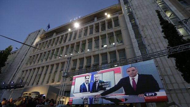 People watch the night news on a screen outside the state broadcaster ERT building following its re-launch after two years in Athens on Thursday.