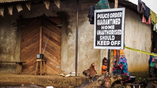A child stands near a sign advising of a quarantined home in Sierra Leone.