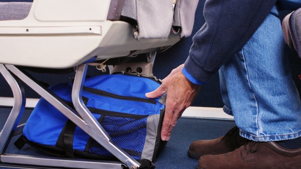 Airplane passenger stowing his carry-on luggage under the seat in front of him.