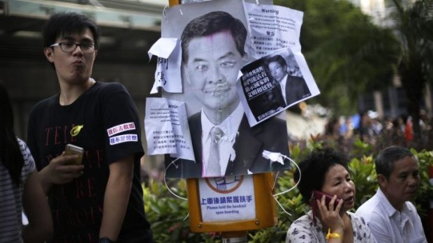 Pro-democracy supporters rest in the streets where a defaced picture of Hong Kong's Chief Executive Leung Chun-ying is plastered on a sign post.