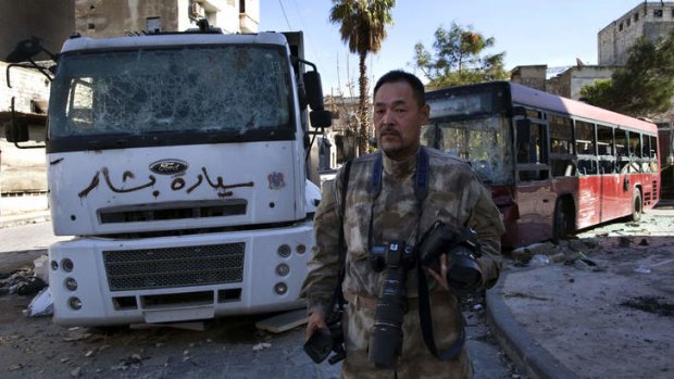 Japanese trucker Toshifumi Fujimoto holds his cameras in front of damaged buses in Aleppo's old city in Syria.