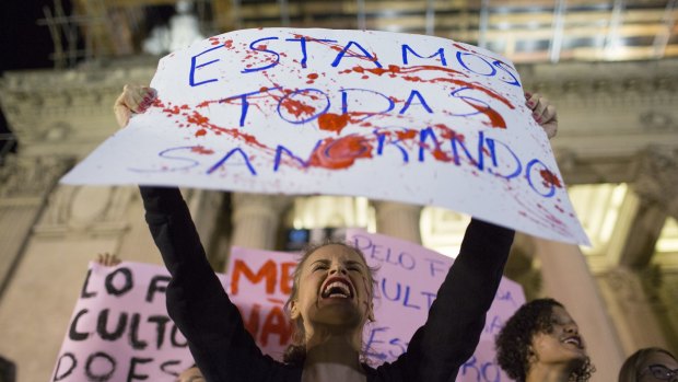 A woman shouts holding a banner that reads in Portuguese "We're all bleeding". 