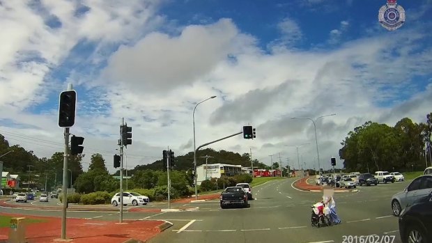 An older woman crosses West Burleigh Road as traffic continues through a green light.