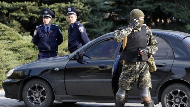 A masked pro-Russian militant stands near Ukrainian police outside a regional government building in Donetsk.