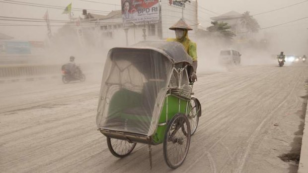 A man wears a mask as he rides a becak, on a road covered with ash from Mount Kelud, in Yogyakarta, on the Indonesian island of Java, on February 14, 2014.