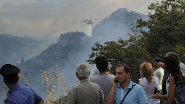 A helicopter sprays water on flames after two Italian air force fighter jets collided during a training mission over Italy and crashed into a hilly, wooded area.