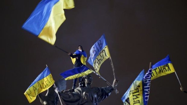 Up in arms: A protester waves a Ukrainian national flag as she stands on a statue during a mass rally at Independence Square in Kiev on Sunday.