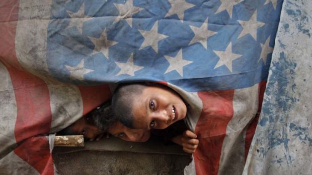A torn US flag helps provide protection - from the elements - for children living in a makeshift shelter in a slum area on the outskirts of Karachi.