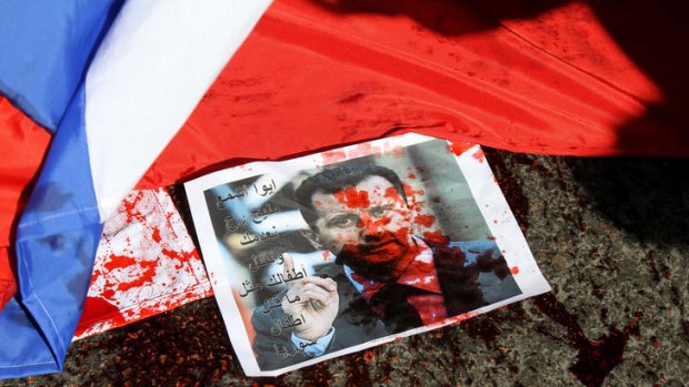A picture of Syria's embattled President Bashar al-Assad sprayed with red paint lies on the ground next to a Russian flag before being set on fire.
