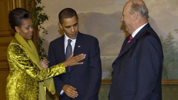 Michelle Obama – watched by Norway’s monarch, King Harald – dusts off  the President’s jacket before he accepts his Nobel Peace Prize.