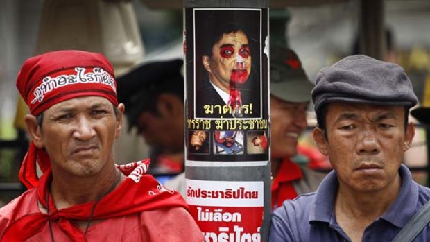 Anti-government demonstrators, standing near a derogatory poster of Thai Prime Minister Abhisit Vejjajiva, listen to Red Shirt leaders speeches.