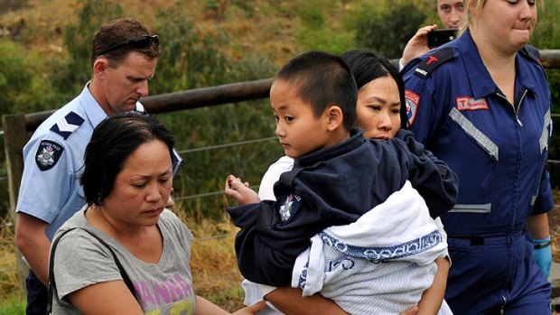 Ryan Pham is carried to safety by his mum after he was pulled from the sodden, swollen creek this morning.