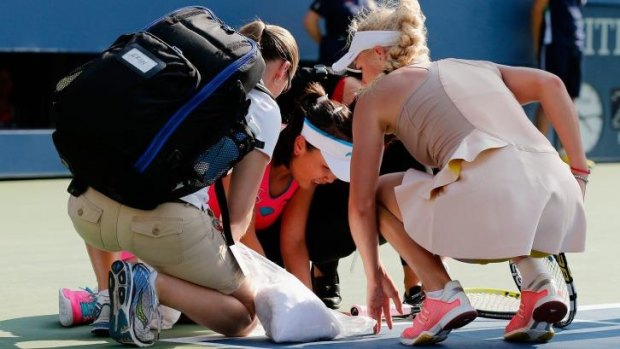 Caroline Wozniacki (R) of Denmark looks on as Shuai Peng (C) of China is tended to by trainers after getting injured in their women's singles 