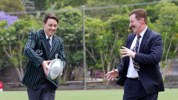 Student Henry Watson passes the footy to Brisbane Boys' College Headmaster Graeme McDonald.