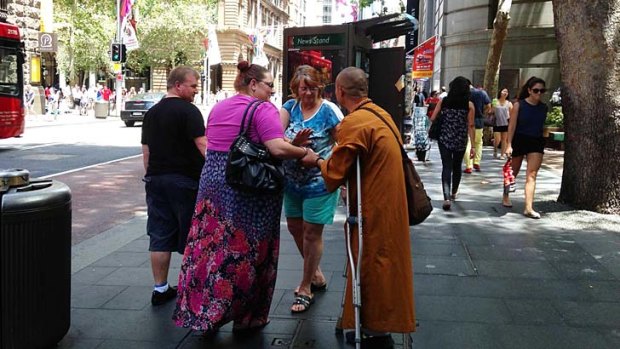 A man dressed as a monk and using crutches approaches people at Martin Place.
