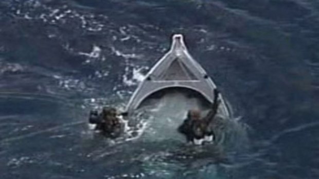 Capsized... divers investigate the overturned boat yesterday. The bodies of two men were found inside.