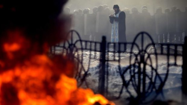 Fears: A priest prays in front of riot police during clashes with anti-government protesters in Kiev. The week of clashes has raised fears of a prolonged civil conflict.