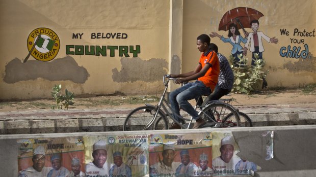Riding bicycles past a mural on a school wall and election posters supporting President Goodluck Jonathan, in Kano, Nigeria on Sunday.