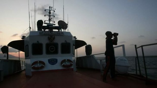 A member of a rescue team looks through binoculars during a search and rescue operation to find the missing Malaysia Airlines Flight MH370