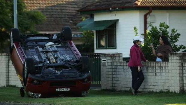Rachna Aggarwal (right) talks to a neighbour near her overturned car on the corner of Clarence street and Fulton Avenue, Constitution Hill, Sydney.