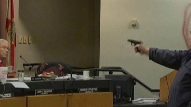 Clay Duke points a gun at a member of a school board.