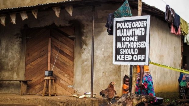 A child stands near a sign advising of a quarantined home in Sierra Leone.