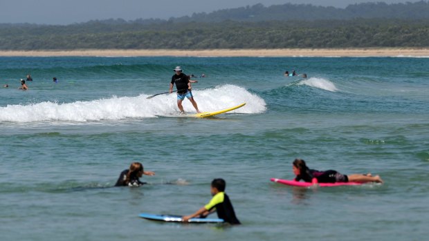 A stand up paddle boarder catches a wave at south Broulee Beach this summer. 