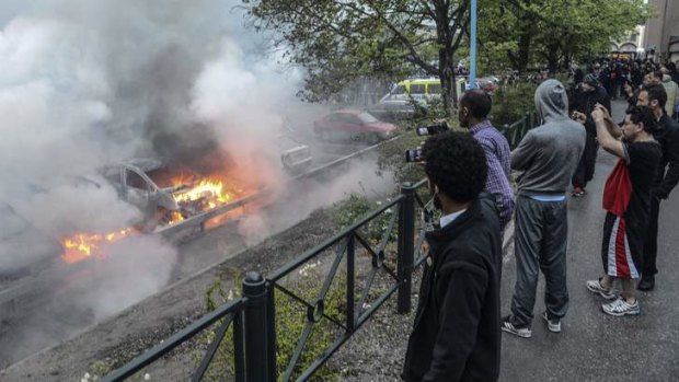 Bystanders take photos of a row of burning cars in the suburb of Rinkeby after youths rioted in several different suburbs around Stockholm.