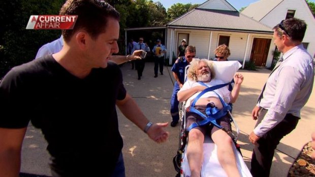 A Current Affair reporter Justin Armsden on the left, watches as notorious conman Peter Foster follows on a stretcher following Tuesday afternoon's discovery of Foster hiding out near Byron Bay.