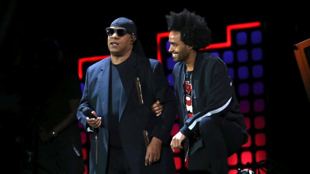 Stevie Wonder, left, kneels on stage next to his son Kwame Morris before performing at the Global Citizen Festival in Central Park on Saturday.
