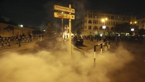Protesters run from smoke from a tear gas canister thrown by riot police.