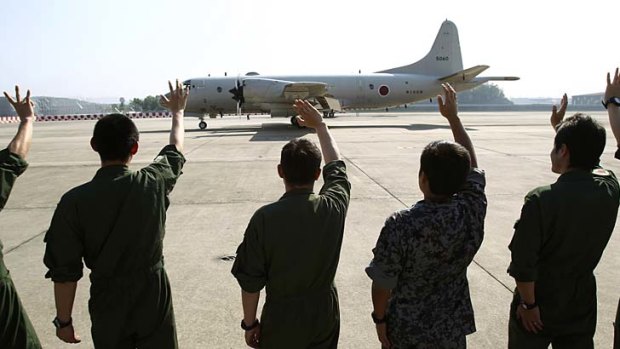 Ground crew members wave to a Japanese Maritime Defence Force P3C patrol plane as it leaves a Royal Malaysian Air Force base in Subang, Malaysia, heading for Australia to join a search and rescue operation for the missing Malaysia Airlines, flight MH370 on Sunday, March 23, 2014.