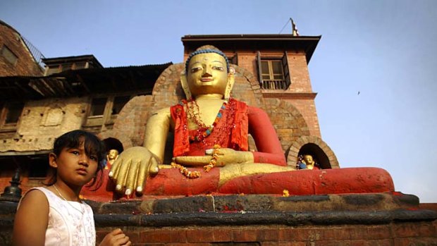 A girl sells goods in front of a Buddha statue at Swyambhu in Kathmandu.