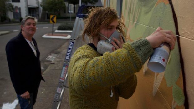 Dale Chaffey watches street artist Birdhat complete a mural on the side of his house  and cafe in Lewisham.